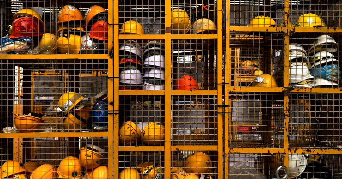 Protective helmets stored behind a safety cage at an industrial workplace.