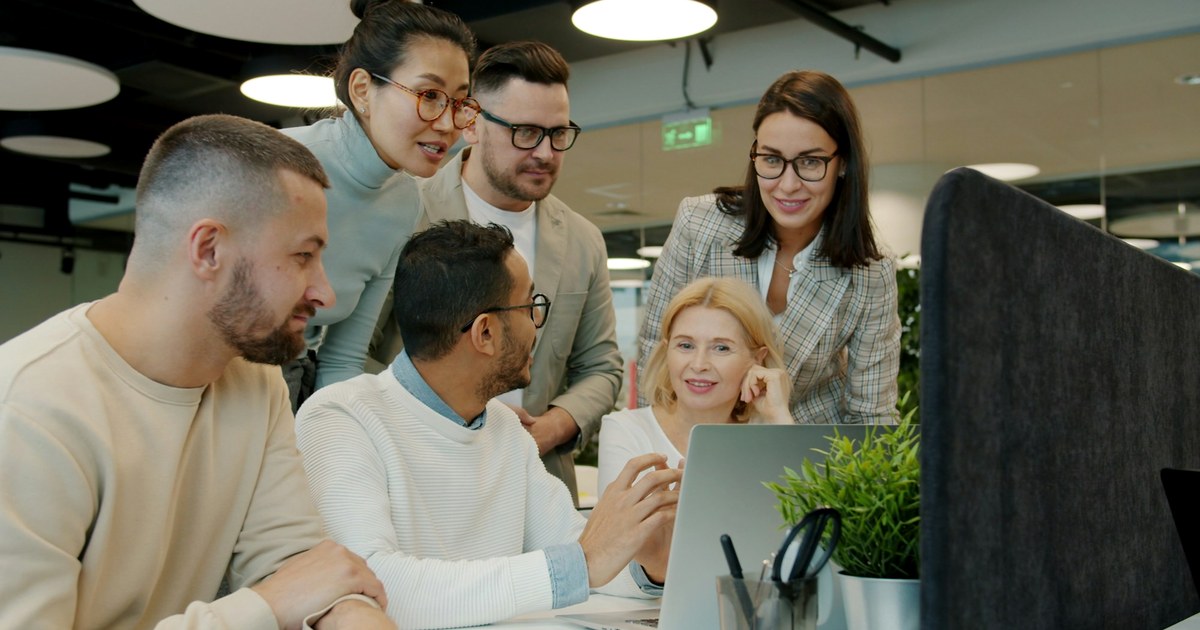 A diverse workplace team collaborating around a laptop during a governance discussion.